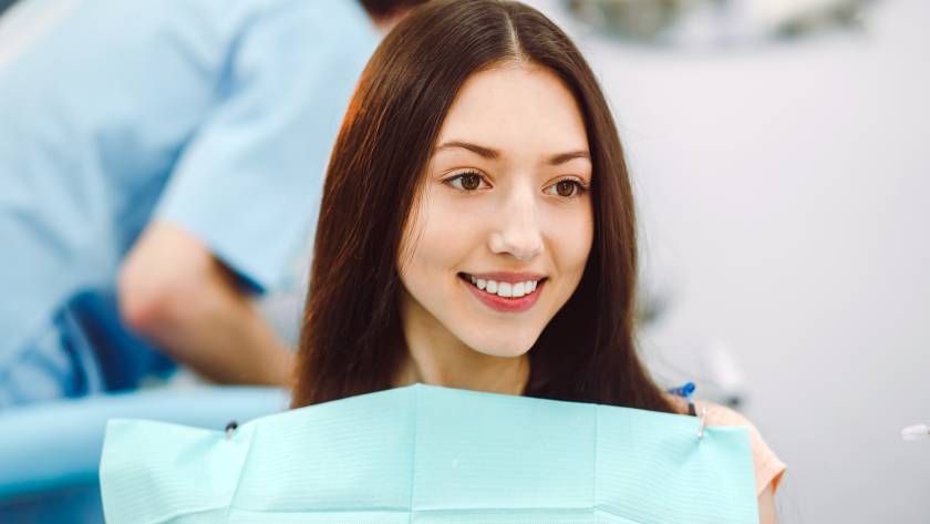Smiling female patient seated in a dental clinic after cosmetic gum depigmentation treatment.