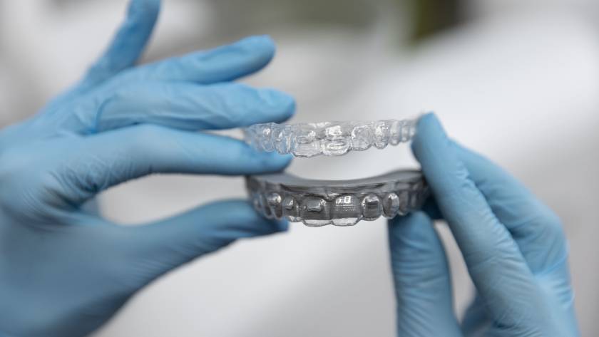 Orthodontist holding clear invisible braces aligners used for correcting overbite, crowded teeth, and gaps between teeth.