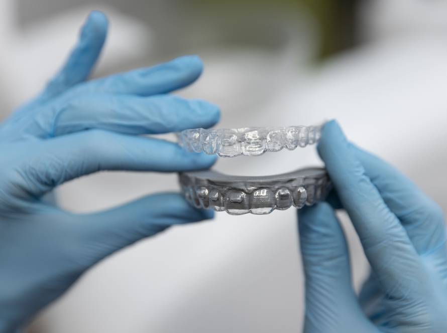 Orthodontist holding clear invisible braces aligners used for correcting overbite, crowded teeth, and gaps between teeth.